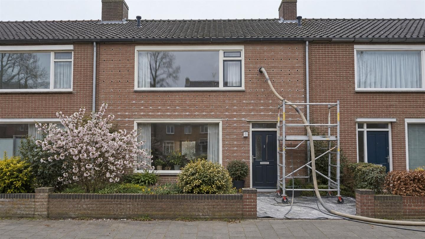 Inblaasslang in een gaatje in de voeg van een bakstenen gevel, met een rolsteiger en al dichtgezette gaatjes
